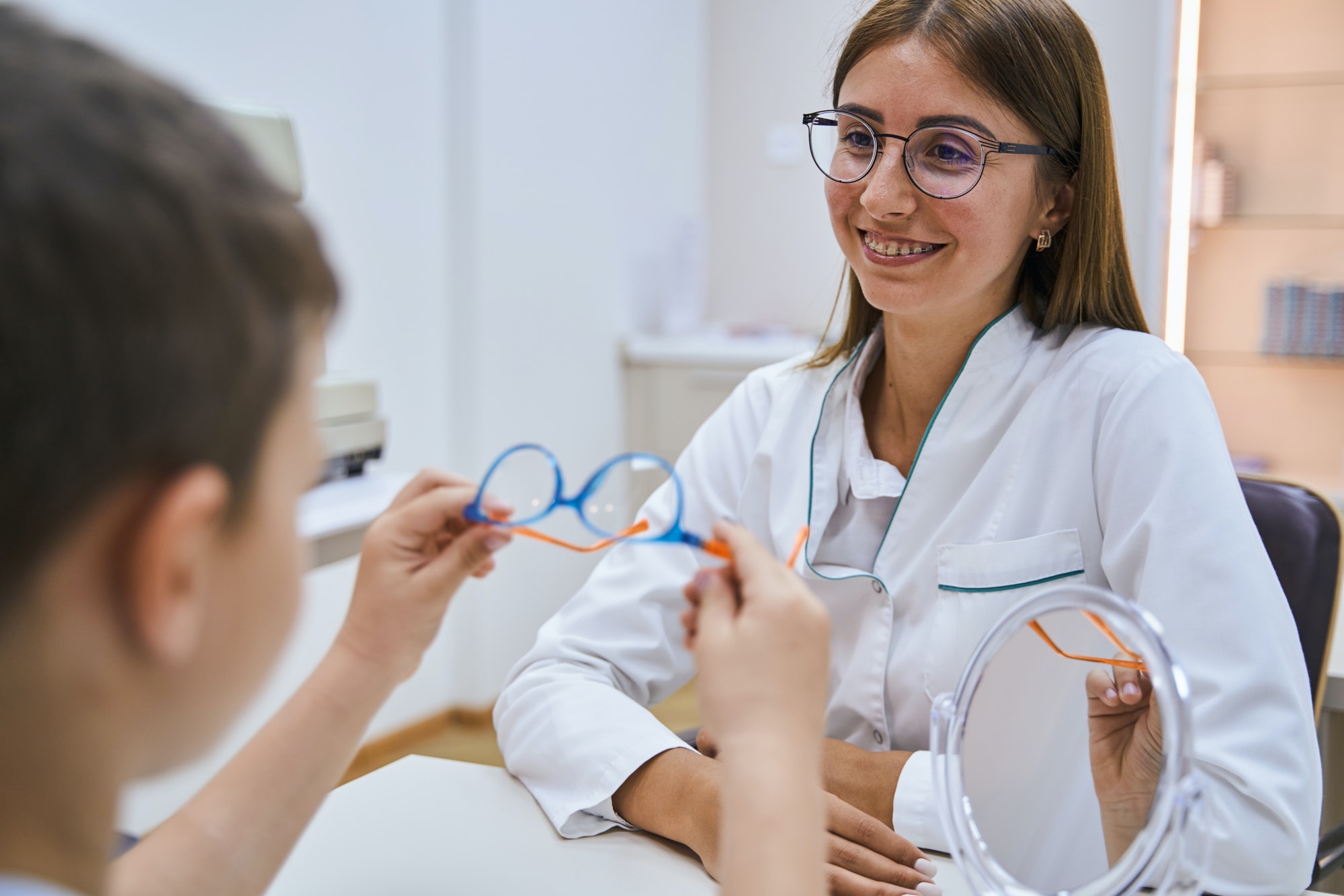 Cheerful optician prescribing glasses to boy in clinic